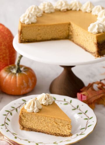 A pumpkin cheesecake on a cake stand with a piece in the foreground.