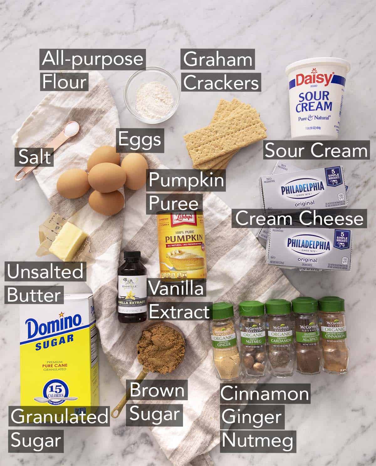 Ingredients to make pumpkin cheesecake on a marble counter.