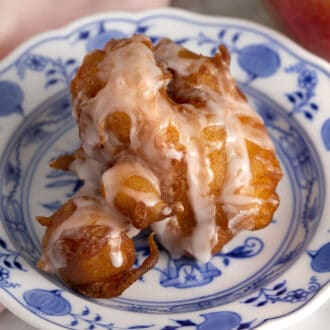 An apple fritter with glaze on a blue and white plate.