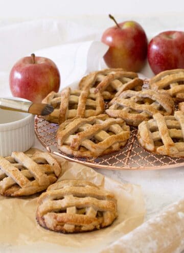 A group of mini apple pies on a copper cooking rack.