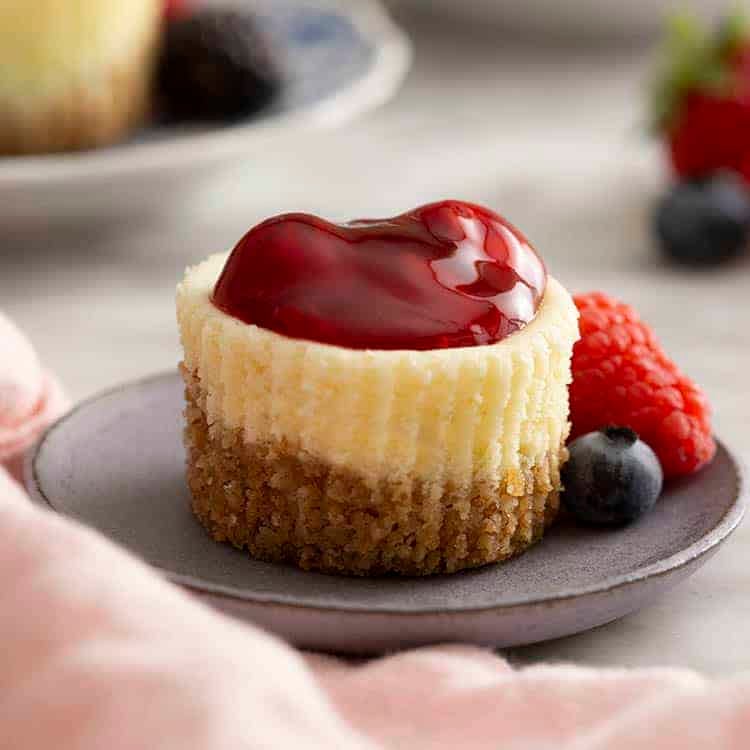 A plate with a mini cheesecake topped with a cherry sauce.