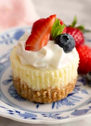 A mini cheesecake topped with whipped cream and berries on blue and white plate.