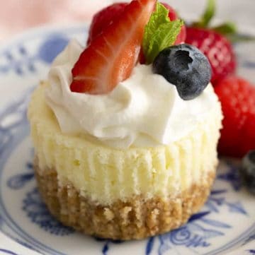 A mini cheesecake topped with whipped cream and berries on blue and white plate.