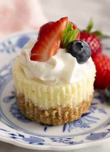 A mini cheesecake topped with whipped cream and berries on blue and white plate.