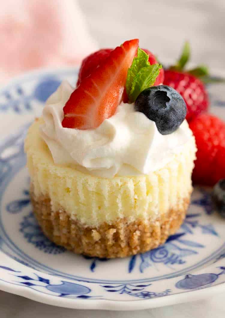 A mini cheesecake topped with whipped cream and berries on blue and white plate.