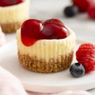 A mini cheesecake topped with cherries on a white plate.