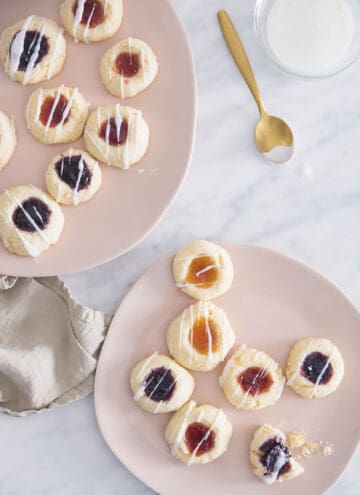 Two soft pink plates filled with thumbprint cookies on a white marble table.