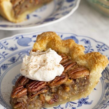 Two pieces of pecan pie on blue and white plates on a marble table.
