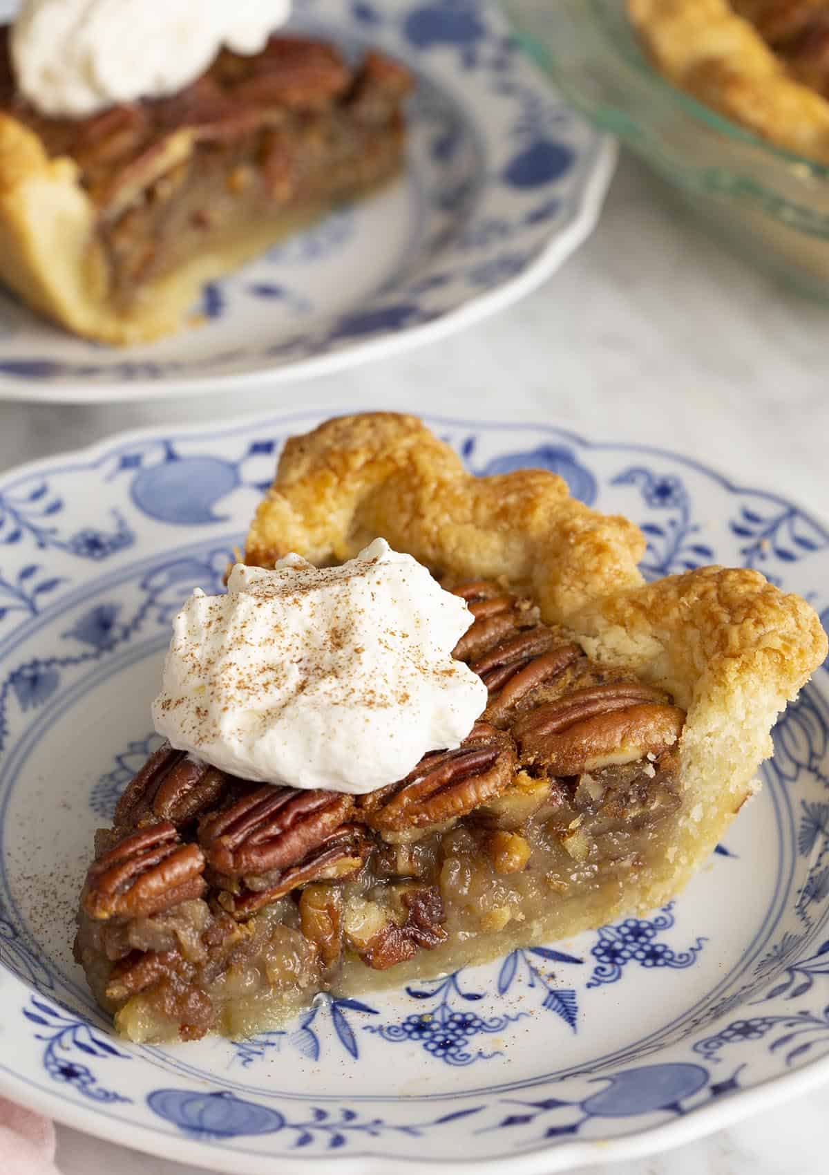 Two pieces of pecan pie on blue and white plates on a marble table.