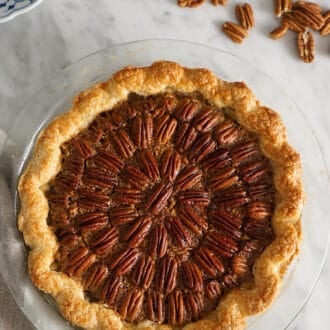 A pecan pie next to some pecans on a table.