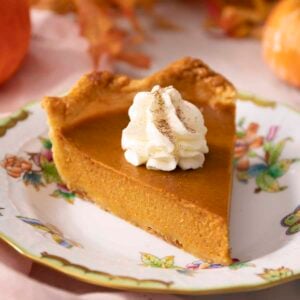 A piece of pumpkin pie with whipped cream on a plate.