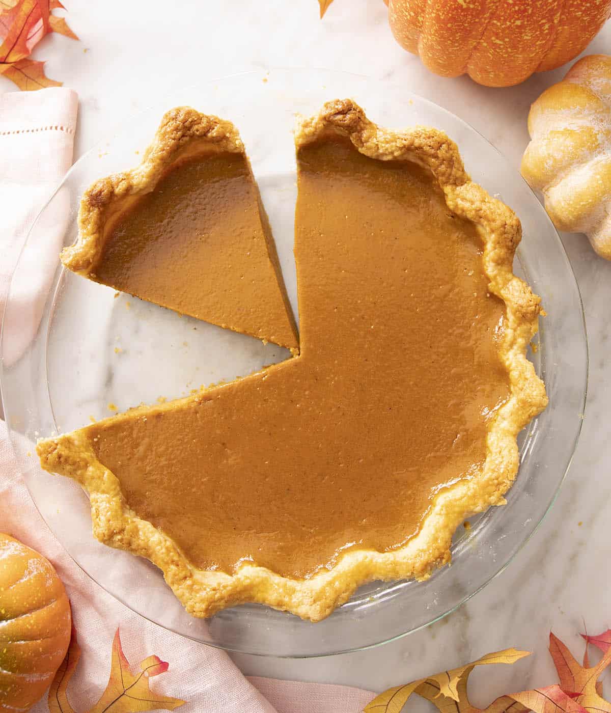 A pumpkin pie in a glass baking dish with a piece cut out.
