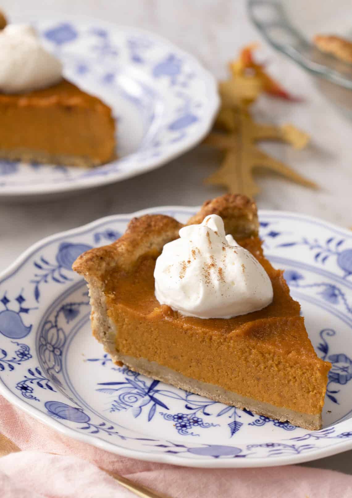 A piece of sweet potato pie with a dollop of whipped cream on a blue and white plate.