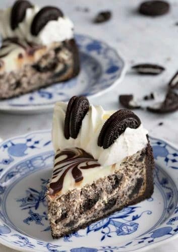 Slice of Oreo cheesecake topped with whipped cream and Oreos on blue and white plates.