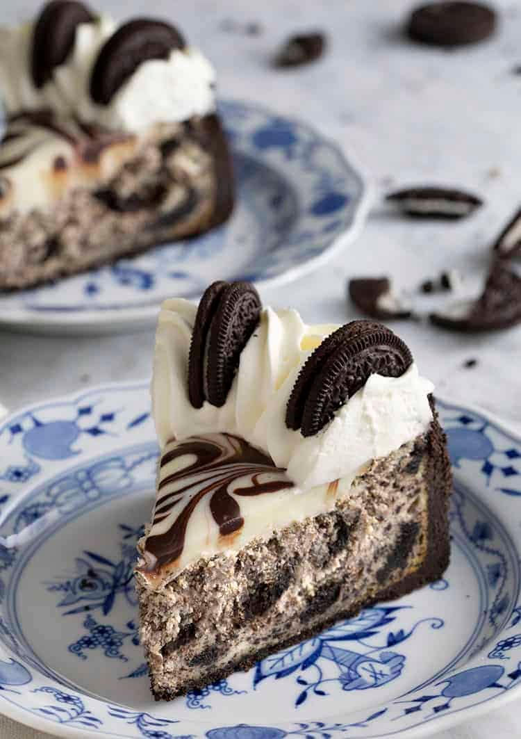 pieces of Oreo cheesecake topped with whipped cream and Oreos on blue and white plates.