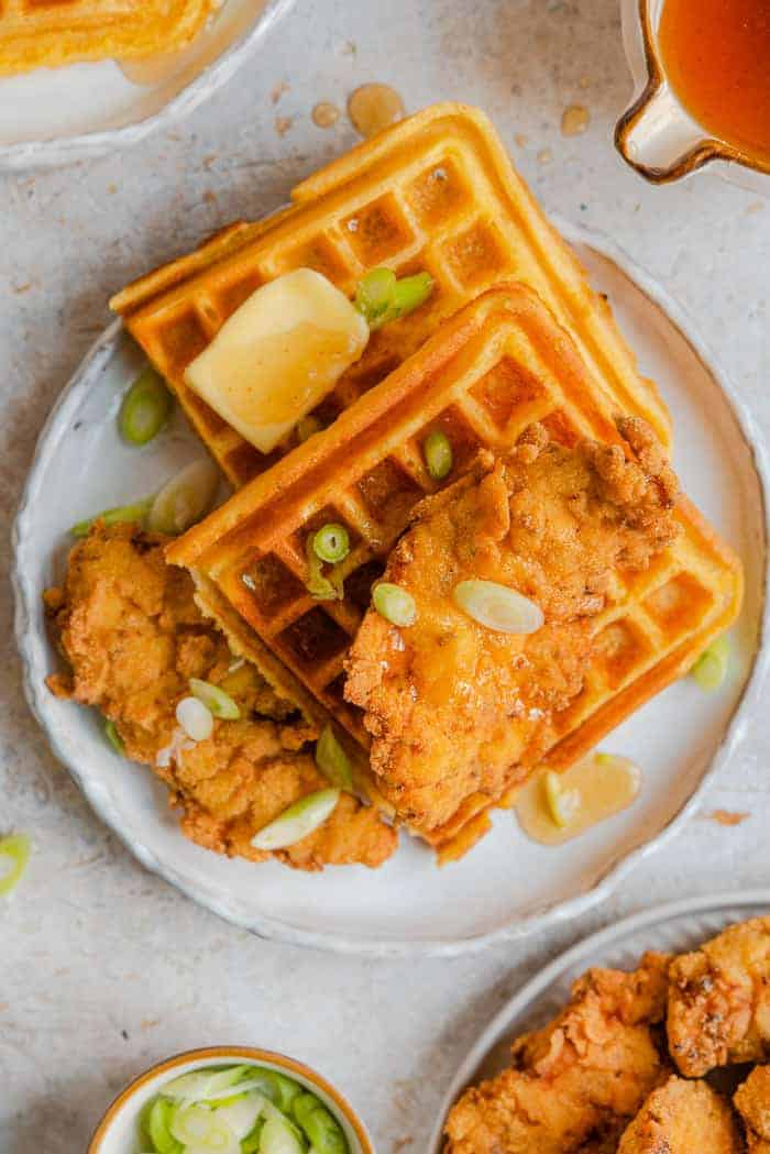 An overhead shot of chicken and waffles with syrup and butter