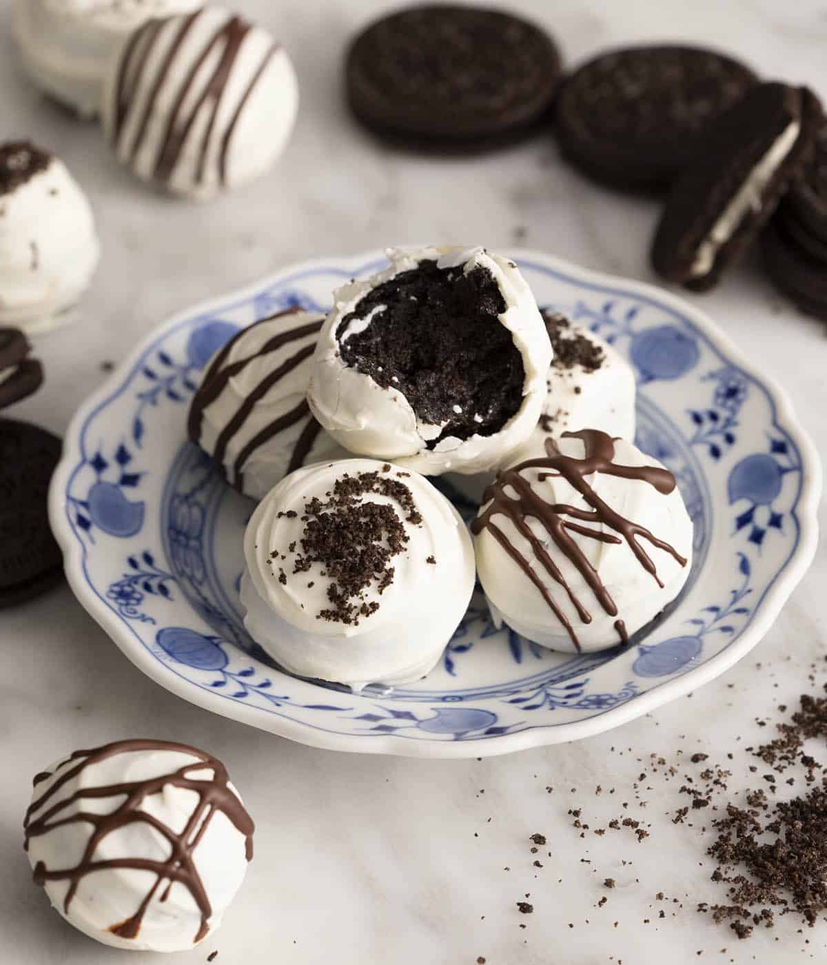 Oreo balls stacked on a blue and white plate. Oreos and balls scattered around.