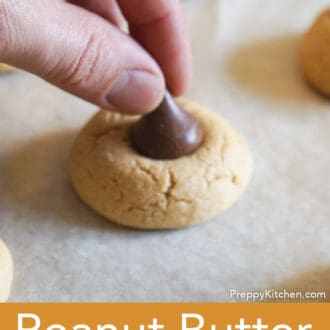 a chocolate kiss being placed onto the peanut butter cookie base