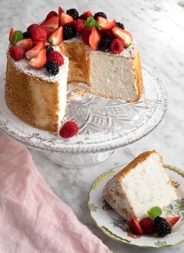 An angel food cake topped with fruit on a crystal cake plate.