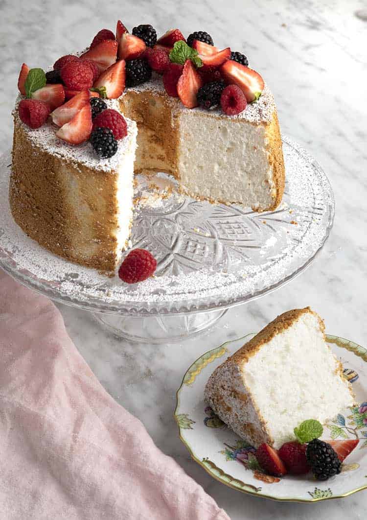 An angel food cake topped with fruit on a crystal cake plate.
