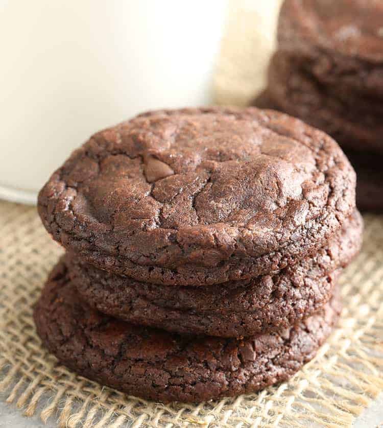 Brownie cookies on a piece of burlap next to a glass of milk.