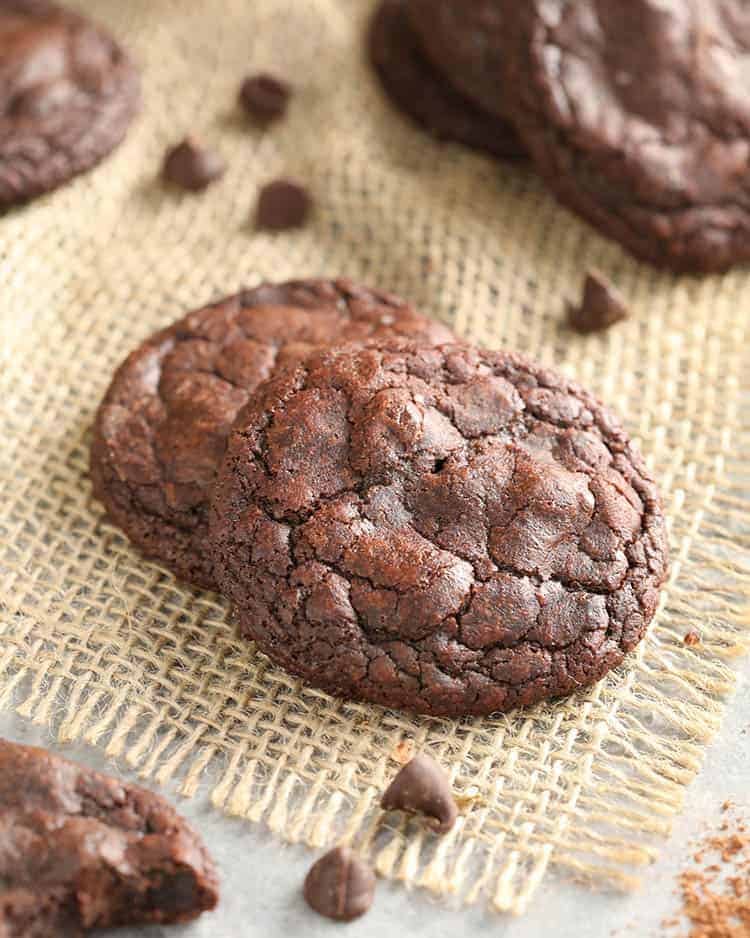 Two brownie cookies next to some chocolate chips.