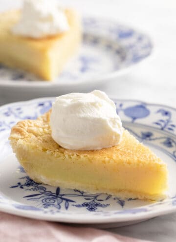 Two pieces of buttermilk pie with whipped cream on a marble table.
