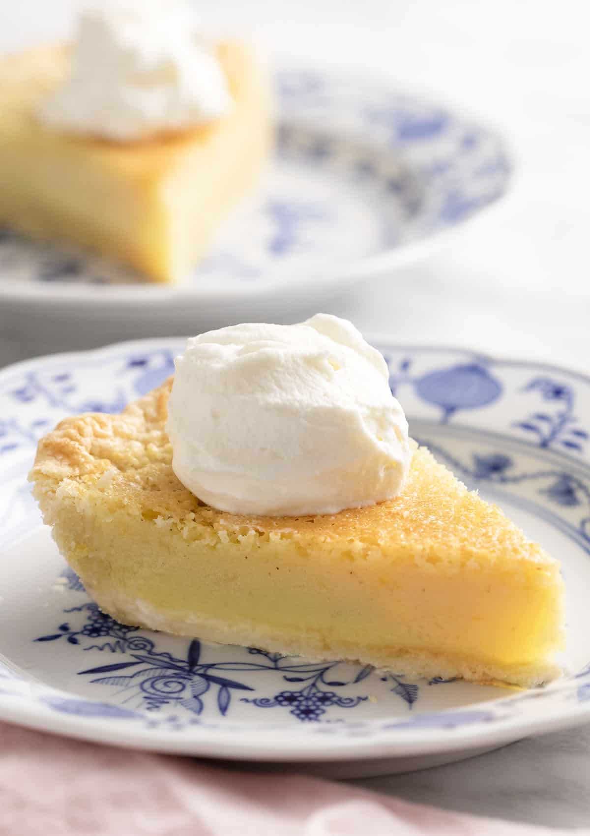 Two pieces of buttermilk pie with whipped cream on a marble table.