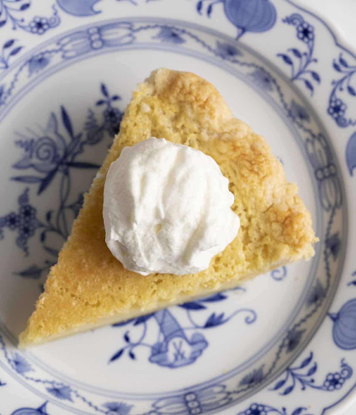 A piece of buttermilk pie topped with whipped cream on a porcelain plate.