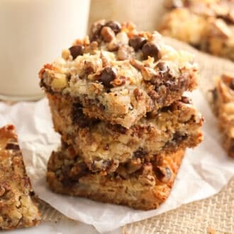 Three magic cookie bars stacked next to a glass of milk.