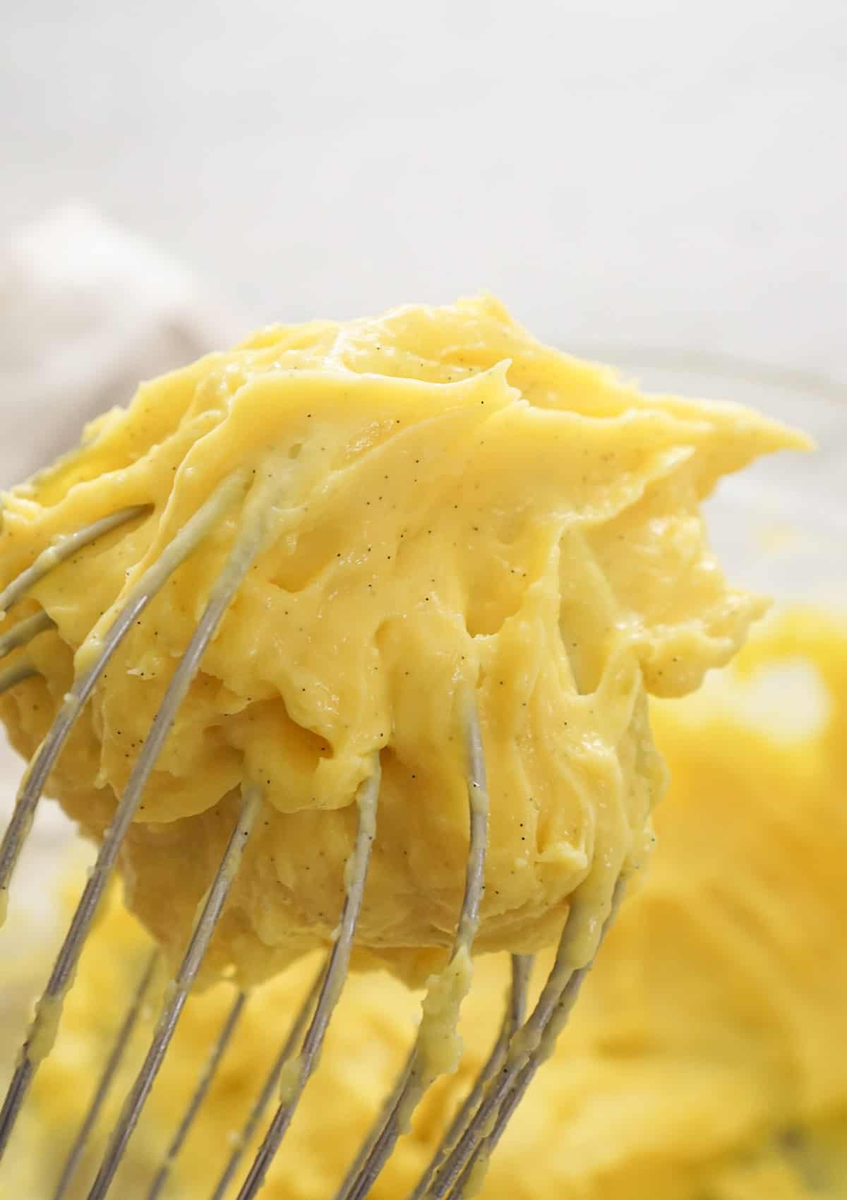 A whisk holding up pastry cream.
