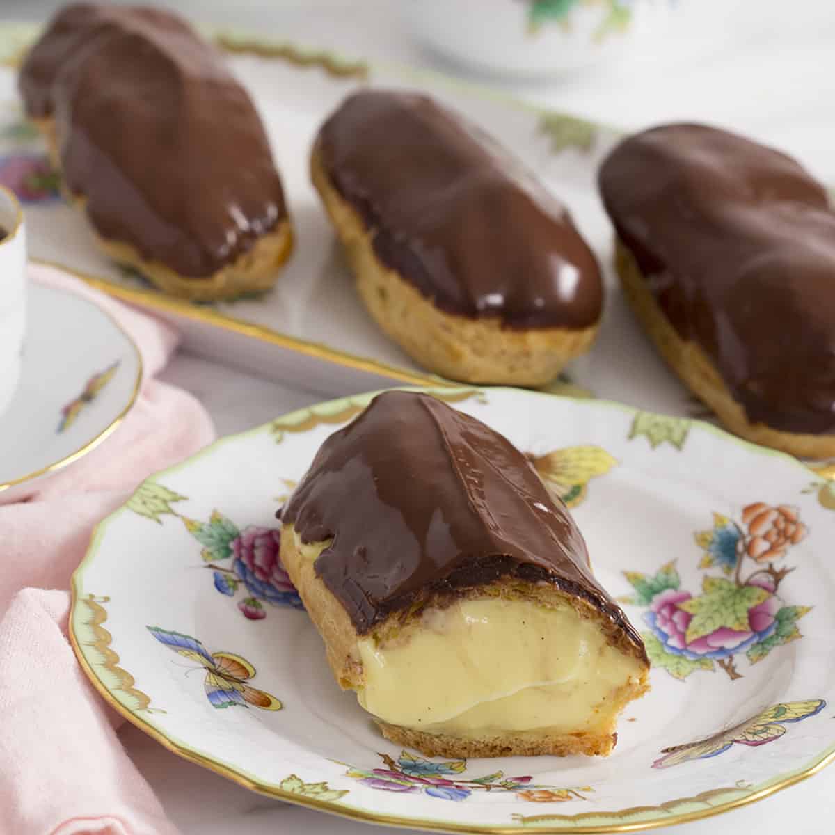 A group of eclairs covered in chocolate and filled with pastry cream