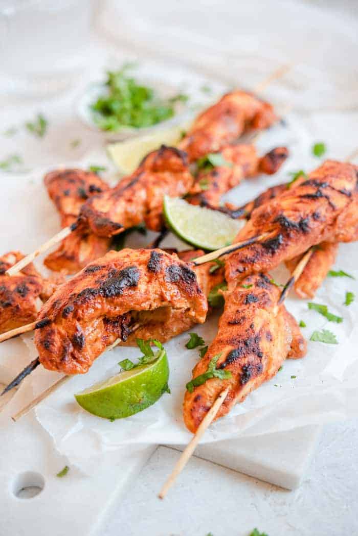 A close up of tandoori chicken skewers with lime wedges