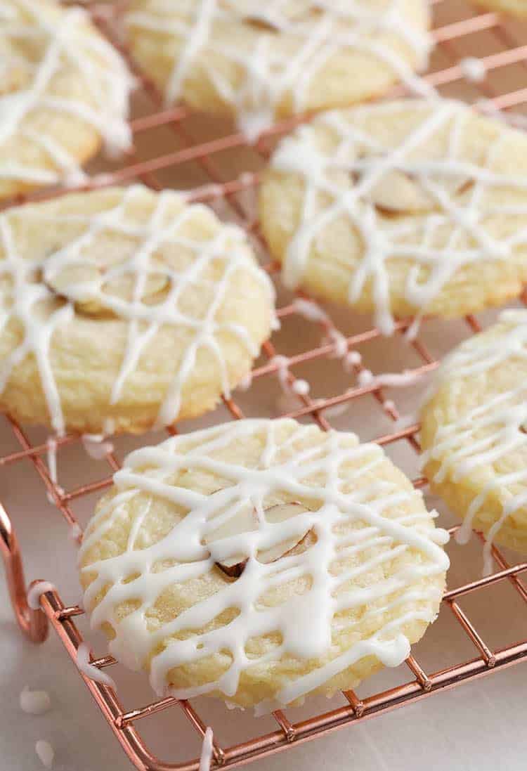 Almond cookies drizzled with glaze on a copper cooling rack