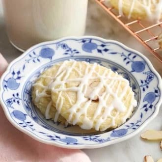 Two almond cookies covered in a drizzle of almond glaze next to a glass of milk.