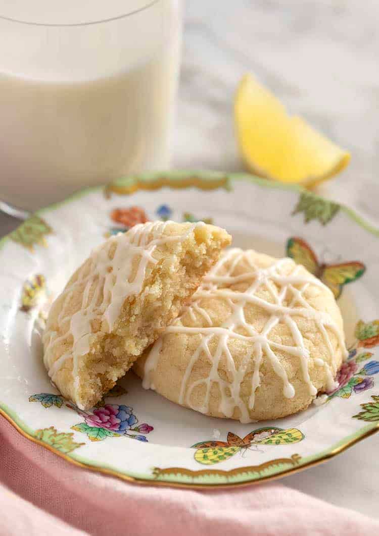 lemon cookies on a porcelain plate next to a glass of milk.