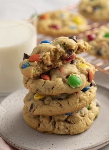 Monster cookies stacked on a grey plate next to a glass of milk.