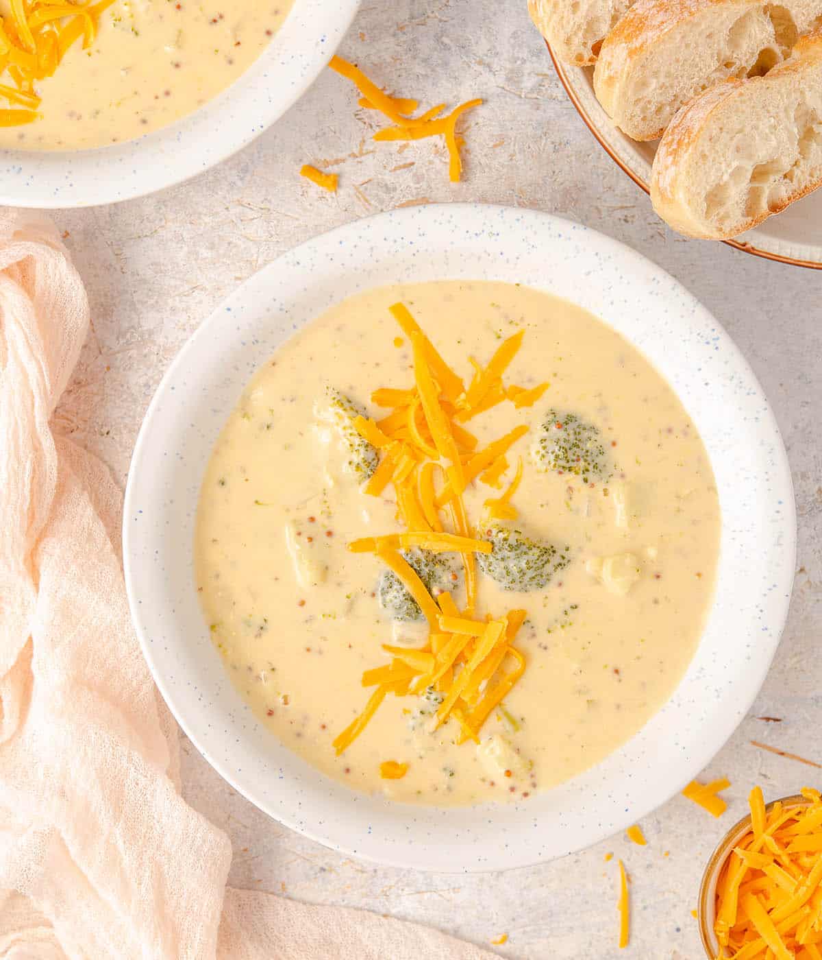 A bowl of broccoli cheese soup with shredded cheddar on top.