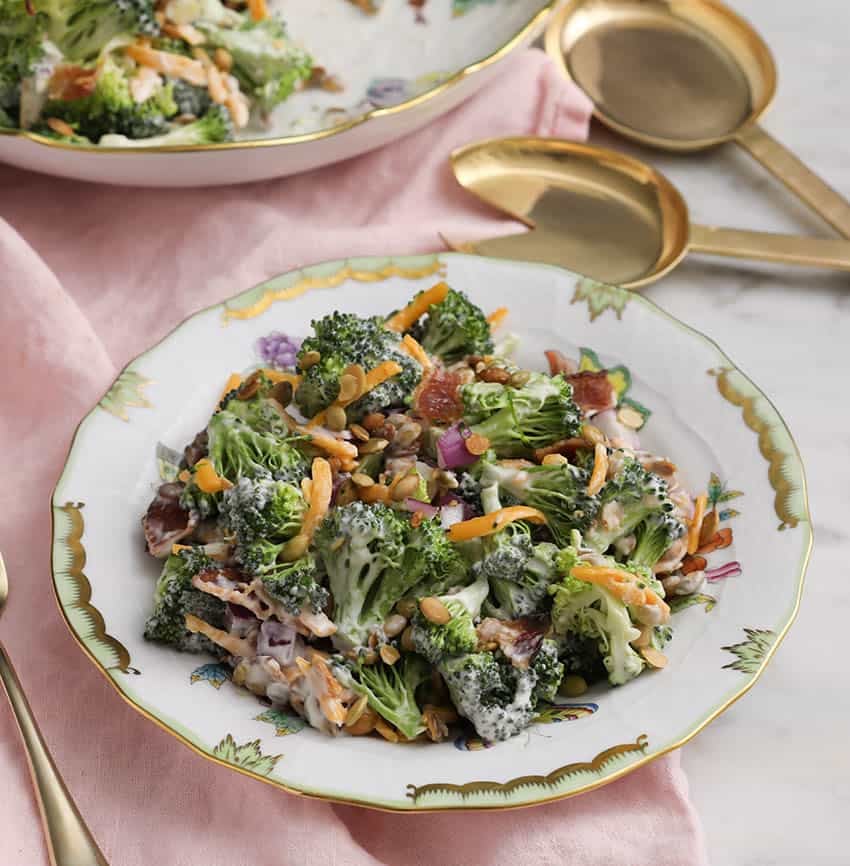 A plate of broccoli salad on a marble table with pink linens.