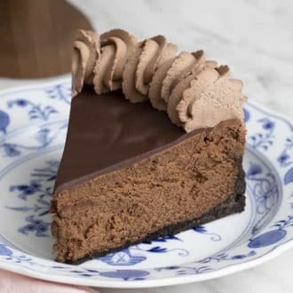 A piece of decadent chocolate cheesecake topped with ganache anc chocolate whipped cream.