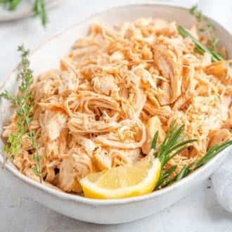 An oval platter of Instant Pot shredded chicken with a lemon wedge, rosemary, and thyme.