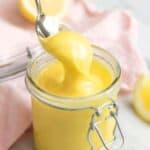 A close up of a spoon picking up some lemon curd from a jar