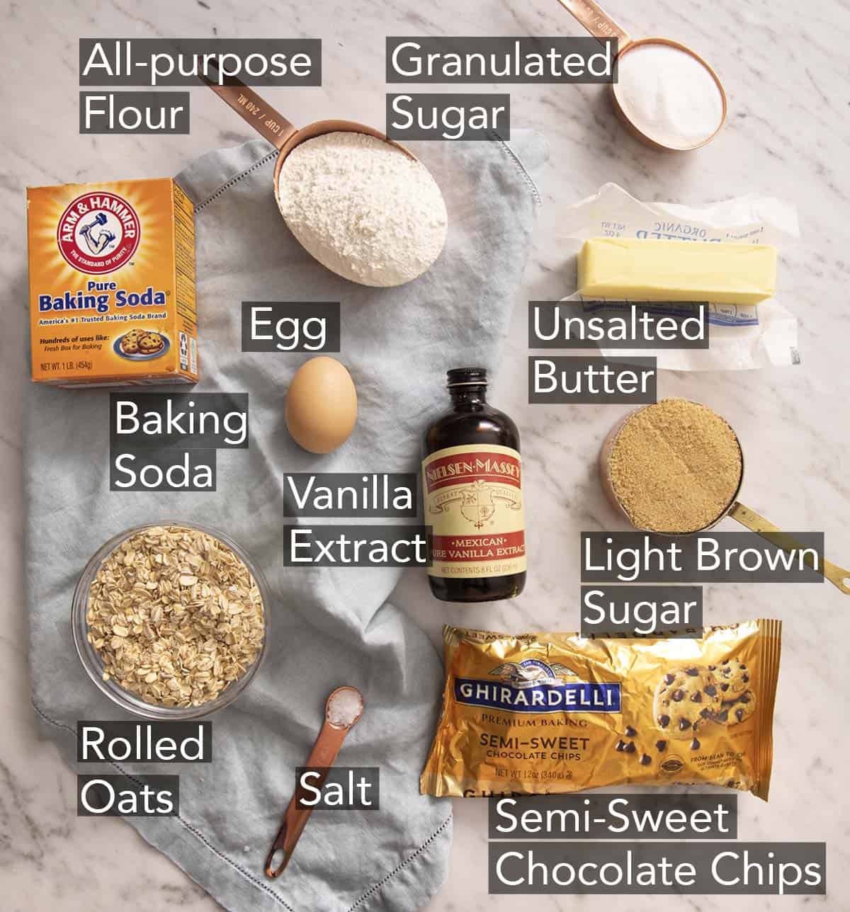 Ingredients to make oatmeal chocolate chip cookies on a marble counter.