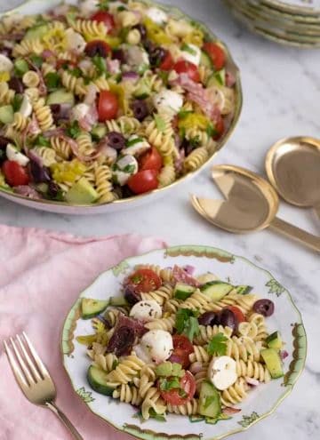 Pasta salad on a porcelain plate nest to a large serving dish.