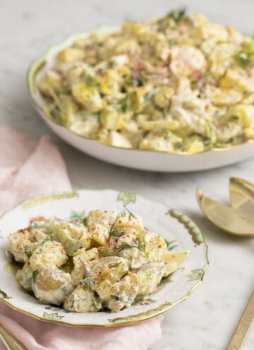 A delicious homemade potato salad on a porcelain plate next to a serving dish.