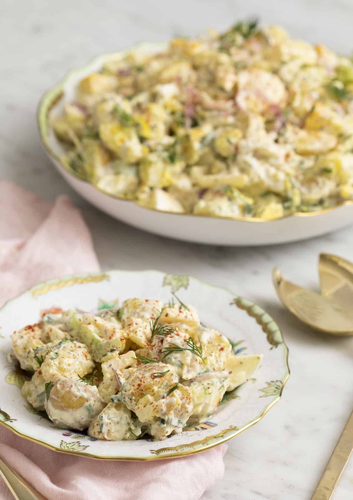 A delicious homemade potato salad on a porcelain plate next to a serving dish.