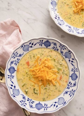 Two bowls of broccoli cheese soup on a marble table.