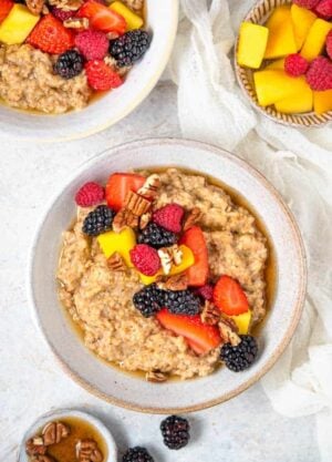 An overhead view of a bowl of Instant Pot steel cut oats topped with fruit and pecans. More toppings in bowls and a second bowl of oats on the side.
