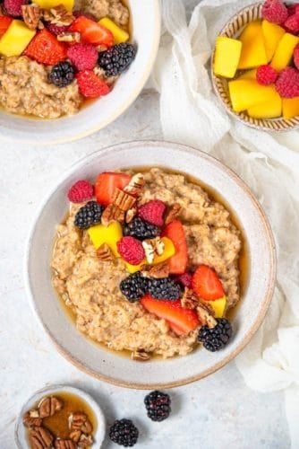 An overhead view of a bowl of Instant Pot steel cut oats topped with fruit and pecans. More toppings in bowls and a second bowl of oats on the side.