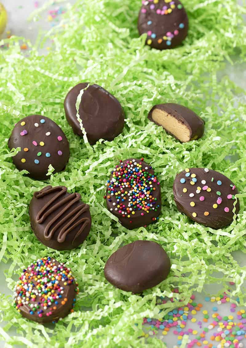Peanut butter eggs covered in chocolate in a bed of green paper grass.